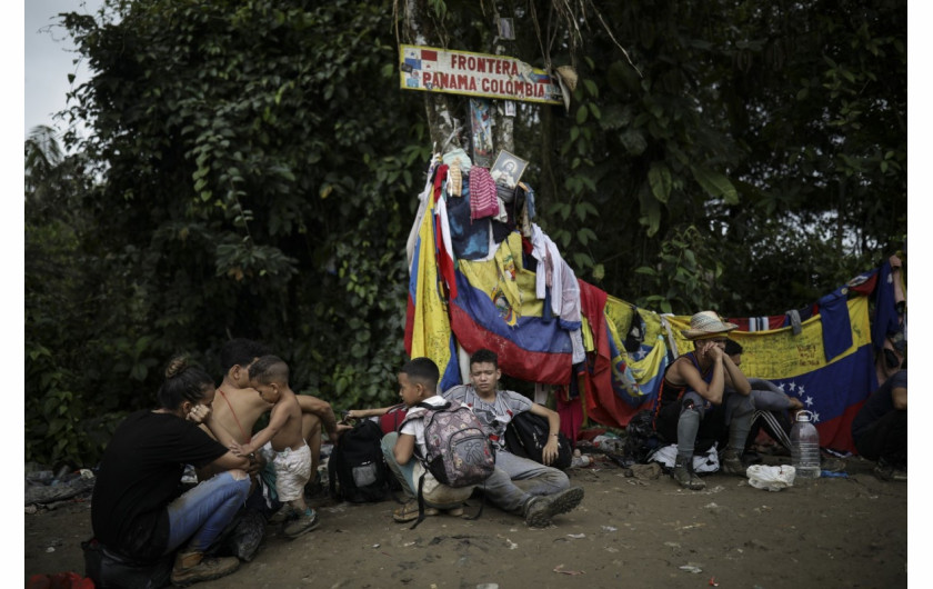 Migranci siedzą pod znakiem oznaczającym granicę Panamy z Kolumbią podczas wędrówki przez Darién Gap, wtorek, 9 maja 2023 r. (AP Photo/Ivan Valencia)
