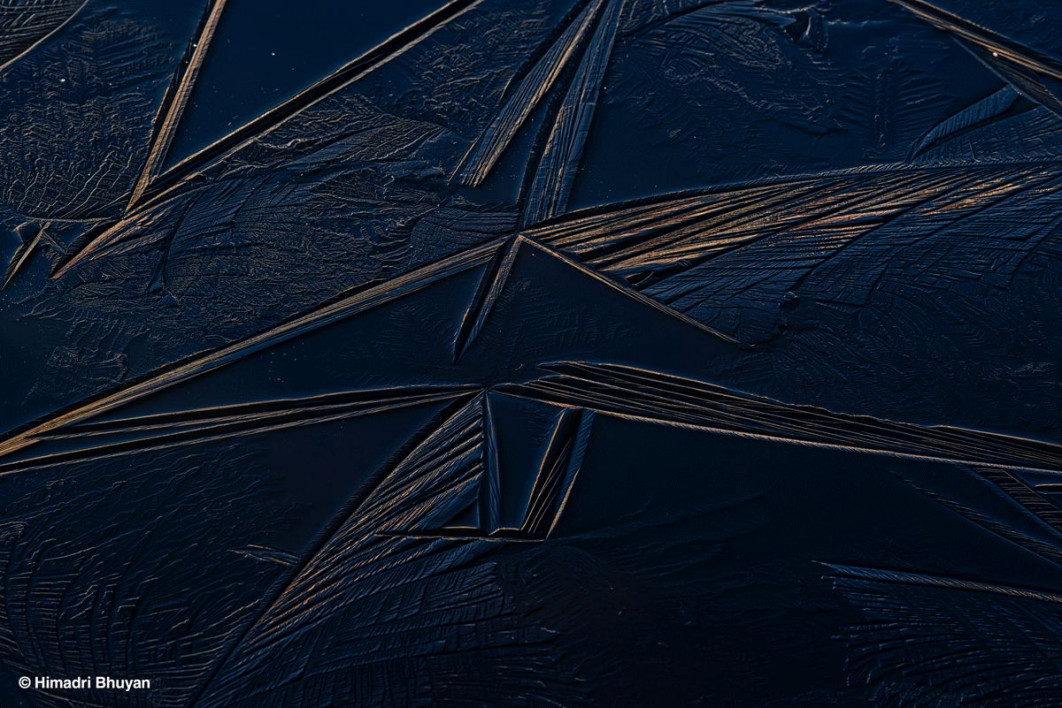 &lt;strong&gt;II Nagroda publiczności, fot. Himadri Bhuyan, Indie&lt;/strong&gt;&lt;br /&gt;&lt;br /&gt;

Wczesnozimowe chłody regionu Arunachal Pradesh w północno-wschodnich Indiach stały się tłem dla tego zdjęcia autorstwa Himadriego Bhuyana, przedstawiającego zamarzniętą taflę jeziora pokrytą misternymi, fraktalnymi wzorami lodu. „Mróz przenikał mnie do kości - dłonie i stopy bolały od zimna - ale te lodowe wzory natychmiast przykuły moją uwagę. Musiałem się zatrzymać i je sfotografować” - wspomina autor. Zdjęcie wykonano w połowie listopada, w pobliżu jeziora Pangateng Tso. Choć scena wydaje się spokojna, kryje w sobie subtelny znak zmieniającego się klimatu.&lt;br /&gt;&lt;br /&gt;

Podczas zamarzania woda rozszerza się, a kryształy lodu formują się od brzegów ku środkowi. Różnice temperatur, obecność zanieczyszczeń czy działanie wiatru mogą tworzyć na powierzchni zjawiskowe wzory - linie, prążki i pęcherzyki powietrza utrwalone w lodzie. Każda z nich stanowi zapis kolejnego etapu procesu zamarzania - widoczną dokumentację zmieniających się warunków.&lt;br /&gt;&lt;br /&gt;

„Tradycyjnie wzory zamarzania były dość przewidywalne - pojawiały się w określonym czasie i miały charakterystyczny kształt, związany z rytmem sezonów” - tłumaczy Bhuyan. „Dziś jednak cykle zamarzania i odwilży stają się coraz bardziej nieregularne. Wpływa to nie tylko na estetykę krajobrazu, ale także na równowagę hydrologiczną i ekologiczną regionu. Zmienione terminy zamarzania mogą zakłócać cykle roślin, życie wodne i dostępność wody w dolinach. Te delikatne formy lodu to nie tylko naturalne dzieło sztuki, lecz także sygnał klimatyczny, przypominający o kruchości i przemianach wysokogórskich ekosystemów w ocieplającym się świecie”.&lt;br /&gt;&lt;br /&gt;

Juror Peter Gibbs podkreślił walory zdjęcia, określając je jako „piękne, abstrakcyjne ujęcie z niezwykle precyzyjnym detalem w strukturze lodu - technicznie doskonałe”.
