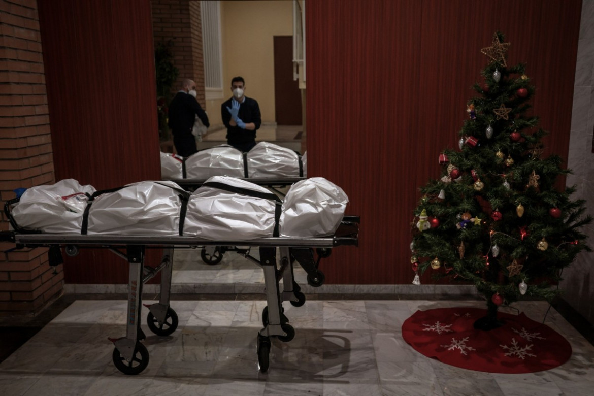 fot. Emilio Morenatti (Associated Press), Pracownicy kostnicy zdejmują odzież ochronną przy wejściu do budynku ozdobionego choinką. Na pierwszym planie ciało osoby podejrzanej o zgon na COVID-19, Barcelona, 23 grudnia 2020 r. / The Pulitzer Prize 2021 for Feature Photography