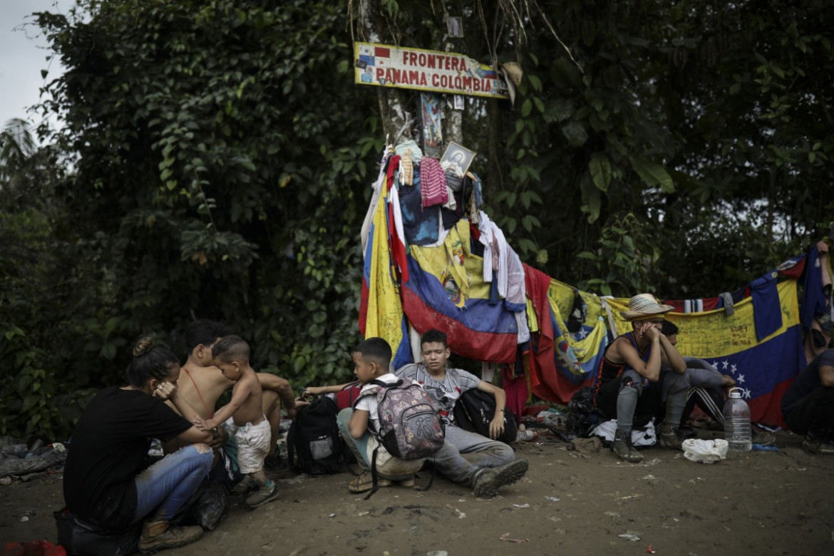 Migranci siedzą pod znakiem oznaczającym granicę Panamy z Kolumbią podczas wędrówki przez Darién Gap, wtorek, 9 maja 2023 r. (AP Photo/Ivan Valencia)