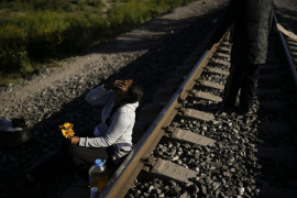 Wenezuelska migrantka śmieje się, żartując ze swoim mężem, który dał jej kilka kwiatów, które zerwał w trawie, gdy czekali wzdłuż linii kolejowych w nadziei na wejście na pokład pociągu towarowego jadącego na północ w Huehuetoca w Meksyku, środa, 20 września 2023 r. (AP Photo/Eduardo Verdugo)