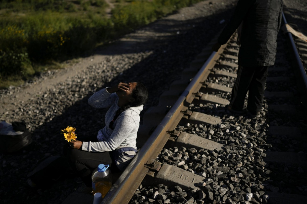 Wenezuelska migrantka śmieje się, żartując ze swoim mężem, który dał jej kilka kwiatów, które zerwał w trawie, gdy czekali wzdłuż linii kolejowych w nadziei na wejście na pokład pociągu towarowego jadącego na północ w Huehuetoca w Meksyku, środa, 20 września 2023 r. (AP Photo/Eduardo Verdugo)