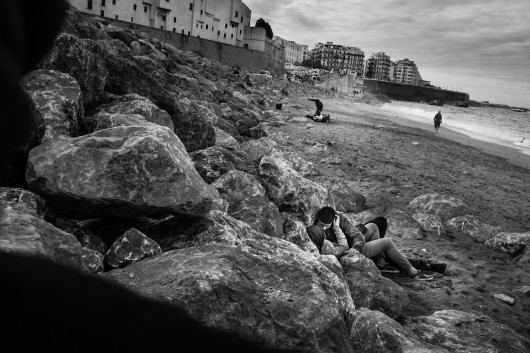 fot. Romain Laurendeau, z projektu Kho, the Genesis of a Revolt, World Press Photo Story of the Year 2020Według raportu UNESCO, 72% Algierczyków poniżej 30 roku życia jest bezrobotnych. Wydarzenia „Czarnego października” z 1988 r., pozostały w pamięci Algierczyków i nadal wzbudzają gniew.  Brutalnie reakcja władzy i  żniwo ponad 500 zabitych w ciągu pięciu dni zapoczątkowały okres zwany „czarną dekadą” przemocy i niepokojów. Po trzydziestu latach skutki tych wydarzeń są nadal obecne. Wysokie bezrobocie prowadzi do frustracji w codziennym życiu, a wielu młodych ludzi czuje się odłączonych od państwa i jego instytucji. W biednych dzielnicach klasy robotniczej, takich jak Bab el-Oued w Algierze, młodzi ludzie szukają schronienia w diki (prywatnych miejscach), które są dla nich „bańkami wolności”, z  dala od spojrzenia społeczeństwa i konserwatywnych wartości społecznych. Jednak to kruche poczucie wspólnoty i solidarności często nie wystarcza, aby złych warunkach życia. W lutym 2019 r. tysiące młodych ludzi z dzielnic robotniczych ponownie wyszło na ulice, co stało się ogólnokrajowym wyzwaniem pod rządami długoletniego prezydenta Abdelaziza Boutefliki.Kho w potocznym języku Afryki oznacza „brat”. Opowiada o genezie buntu. Jest to historia głębokiego niepokoju młodych, którzy znajdują odwagę by rzucić wyzwanie dotychczasowym autorytetom i stają się inspiracją dla reszty populacji. Daje to początek największemu ruchowi protestacyjnemu w Algierii od dziesięcioleci.