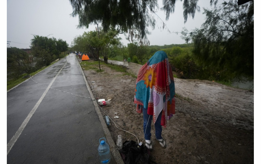 Wenezuelski migrant stoi przykryty folią podczas pisania SMS-a na brzegu Rio Grande w Matamoros w Meksyku, sobota, 13 maja 2023 r. (AP Photo/Fernando Llano)