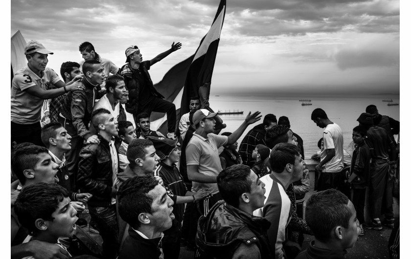 fot. Romain Laurendeau, z projektu Kho, the Genesis of a Revolt, World Press Photo Story of the Year 2020Według raportu UNESCO, 72% Algierczyków poniżej 30 roku życia jest bezrobotnych. Wydarzenia „Czarnego października” z 1988 r., pozostały w pamięci Algierczyków i nadal wzbudzają gniew.  Brutalnie reakcja władzy i  żniwo ponad 500 zabitych w ciągu pięciu dni zapoczątkowały okres zwany „czarną dekadą” przemocy i niepokojów. Po trzydziestu latach skutki tych wydarzeń są nadal obecne. Wysokie bezrobocie prowadzi do frustracji w codziennym życiu, a wielu młodych ludzi czuje się odłączonych od państwa i jego instytucji. W biednych dzielnicach klasy robotniczej, takich jak Bab el-Oued w Algierze, młodzi ludzie szukają schronienia w diki (prywatnych miejscach), które są dla nich „bańkami wolności”, z  dala od spojrzenia społeczeństwa i konserwatywnych wartości społecznych. Jednak to kruche poczucie wspólnoty i solidarności często nie wystarcza, aby złych warunkach życia. W lutym 2019 r. tysiące młodych ludzi z dzielnic robotniczych ponownie wyszło na ulice, co stało się ogólnokrajowym wyzwaniem pod rządami długoletniego prezydenta Abdelaziza Boutefliki.Kho w potocznym języku Afryki oznacza „brat”. Opowiada o genezie buntu. Jest to historia głębokiego niepokoju młodych, którzy znajdują odwagę by rzucić wyzwanie dotychczasowym autorytetom i stają się inspiracją dla reszty populacji. Daje to początek największemu ruchowi protestacyjnemu w Algierii od dziesięcioleci.