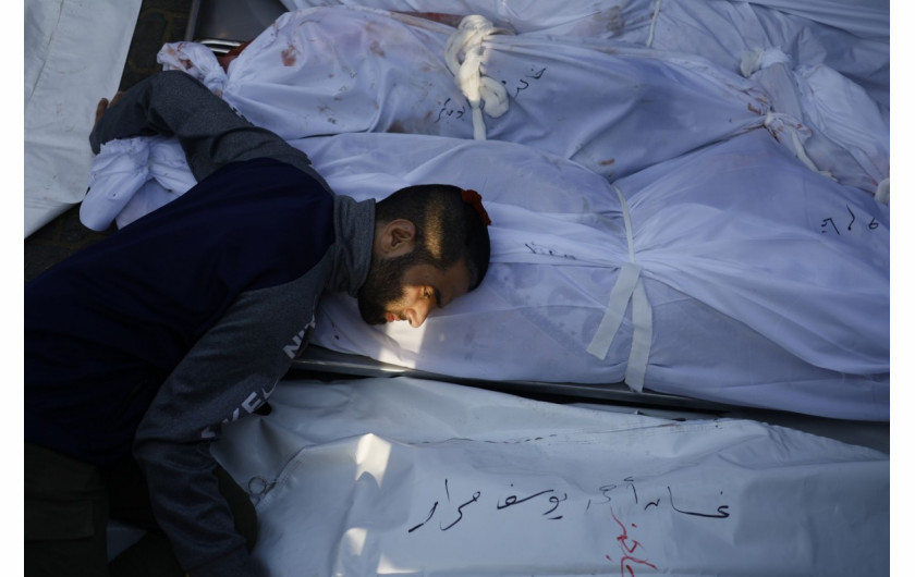 Dzień się kończy, gdy ocalały z izraelskiego nalotu na południową Gazę, który został wysiedlony z miasta Gaza i szukał schronienia u rodziny w mieście Khan Younis, kładzie głowę na zwłokach krewnej o imieniu Tamam, która leży obok innych członków rodziny, którzy zginęli w ataku, szpital Nasser, Khan Younis, Gaza 24 października 2023 r. Napis na dole zdjęcia brzmi: Ghasan Ahmed Youssef Murad. (Zdjęcie Mohammed Salam).