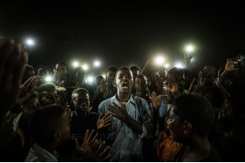 fot. Yasoyushi Chiba, Chartuma<br></br><br></br>Sudan 19 czerwca. Młody człowiek, recytuje wiersz, podczas gdy protestujący nawołują do wprowadzenia cywilnych rządów. Już od grudnia 2018r przez Atbarę przechodzi fala protestów, ludzie maja dość rosnącej ceny żywności, domagają się obalenia dyktatury Omara al-Baszira. 11 kwietnia al-Bashir zostaje usunięty ze stanowiska w wyniku zamachu stanu. Protesty trwają nadal, a niezadowolona ludność cywilna domaga się nowej władzy. W konsekwencji 3 czerwca rozlegają się strzały, to wojsko otwiera ogień do nieuzbrojonych protestujacych. Mimo przerw w dostawach energii i blokadzie internetu, ludzie organizują się i nie poddają w stawianiu oporu i walce o nowy porządek. 