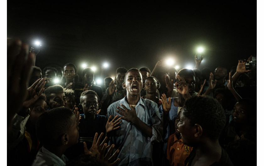 fot. Yasoyushi Chiba, ChartumaSudan 19 czerwca. Młody człowiek, recytuje wiersz, podczas gdy protestujący nawołują do wprowadzenia cywilnych rządów. Już od grudnia 2018r przez Atbarę przechodzi fala protestów, ludzie maja dość rosnącej ceny żywności, domagają się obalenia dyktatury Omara al-Baszira. 11 kwietnia al-Bashir zostaje usunięty ze stanowiska w wyniku zamachu stanu. Protesty trwają nadal, a niezadowolona ludność cywilna domaga się nowej władzy. W konsekwencji 3 czerwca rozlegają się strzały, to wojsko otwiera ogień do nieuzbrojonych protestujacych. Mimo przerw w dostawach energii i blokadzie internetu, ludzie organizują się i nie poddają w stawianiu oporu i walce o nowy porządek. 
