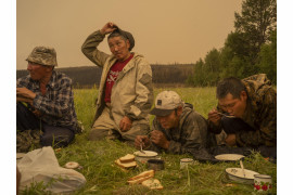 fot. Nanna Heitmann, z cyklu "As Frozen Land Burns", nagroda w okręgu europejskim

<br><br>

1 lipca 2021 r. w Magarasie, w środkowej części Jakucji, na Syberii, w Rosji, ochotnicy z lokalnej straży pożarnej robią sobie przerwę na posiłek.

<br><br>

Sacha, znana również jako Jakucja, rozciągająca się na obszarze ponad trzech milionów kilometrów kwadratowych na dalekim północnym wschodzie Federacji Rosyjskiej, doświadczyła w 2021 r. niszczycielskich pożarów, poważnego zanieczyszczenia dymem i topnienia wiecznej zmarzliny. Według danych Greenpeace Rosja do połowy sierpnia pożary spustoszyły ponad 17,08 mln hektarów - to więcej niż obszary spalone przez pożary w Grecji, Turcji, Włoszech, USA i Kanadzie razem wzięte. Program Monitorowania i Oceny Arktyki donosi, że Arktyka ogrzewa się szybciej niż wynosi średnia światowa.

