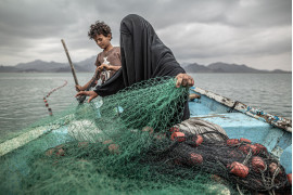 fot. Pablo Tosco, Argentyna, "Yemen: Hunger, Another War Wound", 1 miejsce w kategorii Contemporary issues - zdjęcie pojedyncze / World Press Photo 2021<br></br><br></br>Fatima i jej syn przygotowują sieć rybacką na łodzi w zatoce Khor Omeira w Jemenie, 12 lutego 2020<br></br><br></br>Fatima ma dziewięcioro dzieci, które utrzymuje z rybołówstwa. Chociaż jej wioska została zniszczona przez konflikt zbrojny w Jemenie, Fatima wróciła, by odzyskać środki do życia, kupując łódź za pieniądze zarobione na sprzedaży ryb.<br></br><br></br>Konflikt między muzułmańskimi szyickimi rebeliantami a sunnicką koalicją kierowaną przez Arabię ​​Saudyjską rozpoczął się w 2014 roku i doprowadził do tego, co UNICEF nazwał największym kryzysem humanitarnym na świecie. Na początku 2020 roku około 20,1 miliona ludzi (prawie dwie trzecie populacji) potrzebowało pomocy żywnościowej, a około 80% populacji polegało na pomocy humanitarnej.<br></br><br></br>Blokada koalicji saudyjskiej w Jemenie w latach 2015-2017 nałożyła ograniczenia na import żywności, leków i paliwa. Wynikające z tego niedobory zaostrzyły kryzys humanitarny. W wielu przypadkach głód spowodowany był nie tyle brakiem żywności, ale dlatego, że stała się ona niedostępna cenowo z powodu gwałtownie rosnących kosztów transportu. W 2020 roku konflikt się nasilił, a sytuację pogorszyły: bezprecedensowe ulewne deszcze, w wyniku których około 300 000 osób straciło dach nad głową, plaga szarańczy oraz pandemia COVID-19.