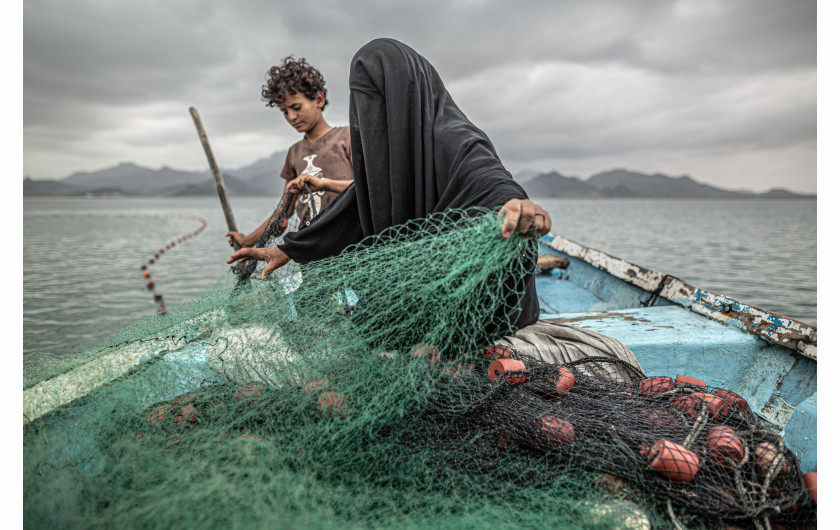 fot. Pablo Tosco, Argentyna, Yemen: Hunger, Another War Wound, 1 miejsce w kategorii Contemporary issues - zdjęcie pojedyncze / World Press Photo 2021Fatima i jej syn przygotowują sieć rybacką na łodzi w zatoce Khor Omeira w Jemenie, 12 lutego 2020Fatima ma dziewięcioro dzieci, które utrzymuje z rybołówstwa. Chociaż jej wioska została zniszczona przez konflikt zbrojny w Jemenie, Fatima wróciła, by odzyskać środki do życia, kupując łódź za pieniądze zarobione na sprzedaży ryb.Konflikt między muzułmańskimi szyickimi rebeliantami a sunnicką koalicją kierowaną przez Arabię ​​Saudyjską rozpoczął się w 2014 roku i doprowadził do tego, co UNICEF nazwał największym kryzysem humanitarnym na świecie. Na początku 2020 roku około 20,1 miliona ludzi (prawie dwie trzecie populacji) potrzebowało pomocy żywnościowej, a około 80% populacji polegało na pomocy humanitarnej.Blokada koalicji saudyjskiej w Jemenie w latach 2015-2017 nałożyła ograniczenia na import żywności, leków i paliwa. Wynikające z tego niedobory zaostrzyły kryzys humanitarny. W wielu przypadkach głód spowodowany był nie tyle brakiem żywności, ale dlatego, że stała się ona niedostępna cenowo z powodu gwałtownie rosnących kosztów transportu. W 2020 roku konflikt się nasilił, a sytuację pogorszyły: bezprecedensowe ulewne deszcze, w wyniku których około 300 000 osób straciło dach nad głową, plaga szarańczy oraz pandemia COVID-19.