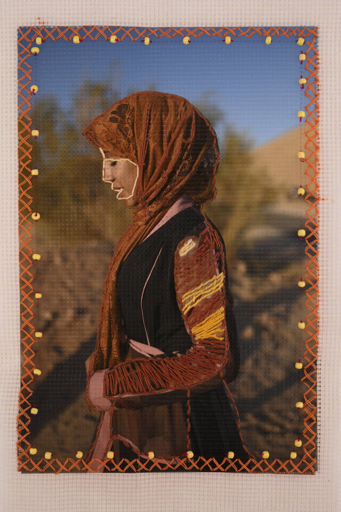 fot. Rehab Eldalil, z cyklu "The Longing of the Stranger Whose Path Has Been Broken"

<br><br>

Zdjęcie Nadii (20 lat), wyhaftowane przez nią i jej kuzynkę Mariam (19 lat), w Świętej Katarzynie na Południowym Synaju w Egipcie, 8 grudnia 2019 r.

<br><br>

Beduini zamieszkują półwysep Synaj od wieków i od dawna spotykają się z dyskryminacją. Nadal uważa się, że byli kolaborantami podczas izraelskiej okupacji Synaju w latach 1967-1982, kiedy to pozostali, by chronić swoją ziemię. Kobiety beduińskie są także źle przedstawiane i stereotypowo traktowane w egipskich mediach. W ramach projektu, który podważa te stereotypy, portrety kobiet z tej społeczności, wydrukowane na tkaninie, zostały wyhaftowane przez nie same, a mężczyźni z tej społeczności dodali odręcznie napisane wiersze. Fotografka jest aktywistką i od 15 lat aktywnie działa na rzecz tej społeczności. 
