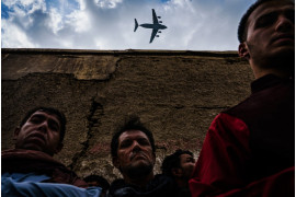 fot. Marcus Yam / LA Times, Wojskowy samolot transportowy przelatuje nad krewnymi i sąsiadami rodziny Ahmadi, zgromadzonej wokół pojazdu zniszczonego przez amerykański atak dronów w Kabulu / Pulitzer Prize 2021 for Breaking News Photography