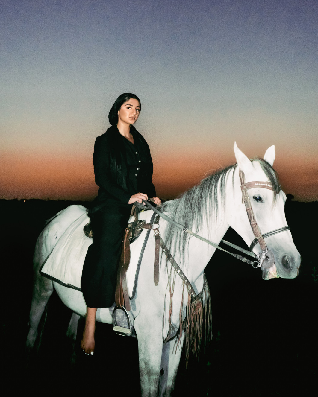 Fot. Bea Dero, "Azadi Freedom" / Female in Focus x Nikon vol. 5<br></br>Autoportret wykonany w Iranie po zabójstwie Mahsy Amini przez irańską policję obyczajową we wrześniu 2022 roku. To zdjęcie jest wyrazem solidarności z ruchem "Kobieta, Życie, Wolność". Opłakując śmierć niewinnych irańskich aktywistów, przedstawiam irańską kobietę w centrum kadru, w świetle reflektorów, na białym koniu o zachodzie słońca, służącym jako symbol nadziei. Nadziei na rewolucję i przyszłość, w której kobiety będą mogły publicznie i z godnością bronić swojej tożsamości.