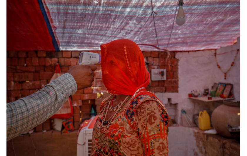 Pracownik służby zdrowia sprawdza temperaturę kobiety podczas akcji szczepień przeciwko koronawirusowi dla pracowników w cegielni w wiosce Kavitha na obrzeżach Ahmedabad w Indiach, 8 kwietnia 2021 r. fot. Amit Dave, Reuters / The Pulitzer Prize 2021 for Feature Photography