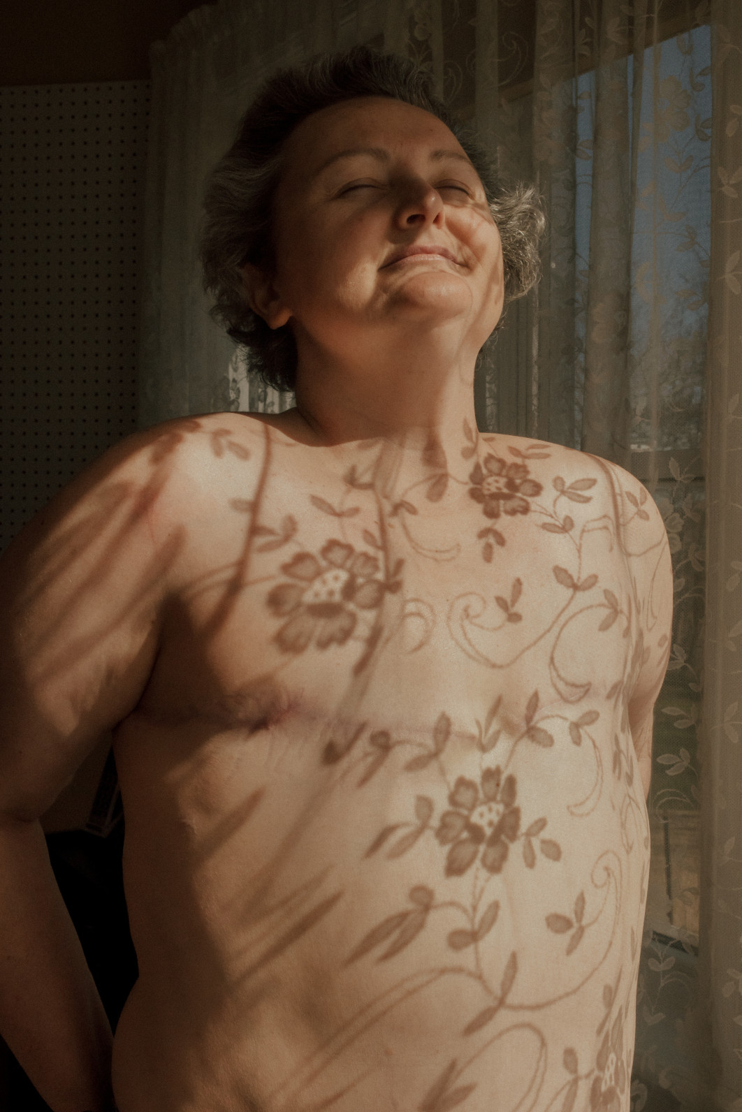 Fot. Hanna Wolf, "Fiona" / Female in Focus x Nikon vol. 5<br></br>Poznałam Fionę w ramach projektu badającego historie matek, które nie mogły trzymać swoich dzieci po urodzeniu. Po traumatycznym porodzie bliźniąt, Fiona stanęła w obliczu druzgocącej diagnozy: rak piersi. Utracone chwile trzymania
noworodków na piersi odbiły się echem, jakiego nigdy nie mogła sobie wyobrazić. Kiedy się spotkaliśmy, sześć miesięcy po mastektomii, Fiona przyznała, że wreszcie jest gotowa, by zostać sfotografowaną ze swoimi bliznami. To, co zaczęło się od braku dotyku, przekształciło się w głęboką podróż pełną żalu, odporności i triumfu.