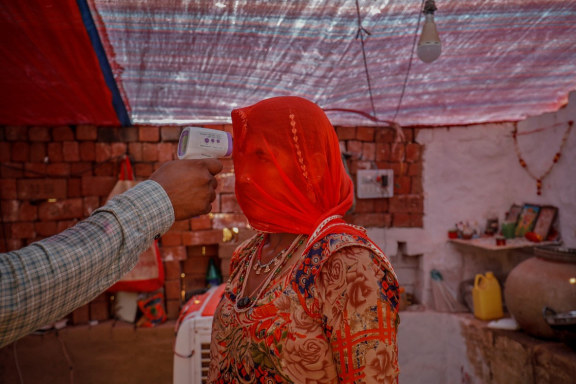 Pracownik służby zdrowia sprawdza temperaturę kobiety podczas akcji szczepień przeciwko koronawirusowi dla pracowników w cegielni w wiosce Kavitha na obrzeżach Ahmedabad w Indiach, 8 kwietnia 2021 r. fot. Amit Dave, Reuters / The Pulitzer Prize 2021 for Feature Photography