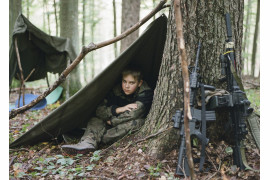 fot. Natalia Kepesz, Polska, z cyklu: "Niewybuch", 3 miejsce w kategorii "Portret - seria zdjęć" / World Press Photo 2021
<br></br><br></br>

Wojskowe obozy letnie dla młodzieży istnieją w Polsce od lat 20. ubiegłego wieku. Młodzi uczestnicy przechodzą przez obozy kondycyjne, poddawani są ciężkim próbom fizycznym i psychicznym, a także uczą się - często na byłych poligonach wojskowych - taktyki, przetrwania, samoobrony i topografii. Uczy się ich także strzelania, używając karabinów pneumatycznych, a czasem replik broni, takich jak karabiny maszynowe i granatniki. Obozy promowane są jako okazja do przeżycia przygody i rekreacji, a także jako zajęcia kształtujące charakter i zachęcające do pracy w grupie. Organizatorzy utrzymują, że uczestnictwo w grach z replikami broni powstrzymuje dzieci przed sięgnięciem po prawdziwą. Z drugiej strony, pojawiają się głosy krytyki, które sugerują, że popularność obozów wynika ze wzrostu nacjonalizmu w Polsce, szczególnie od czasu dojścia do władzy PiS, prawicowej partii populistycznej. Patriotyzm i nacjonalizm odgrywają istotną rolę w edukacji szkolnej.