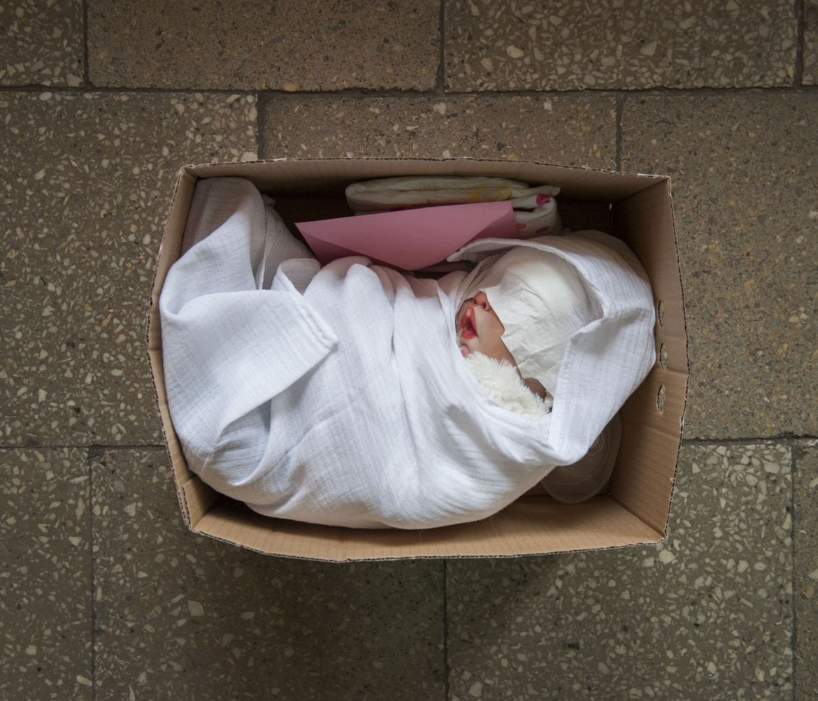 fot.
Karolina Jonderko, Polska, z cyklu: "Reborn", nominacja w kategorii "Projekt długoterminowy" / World Press Photo 2021<br></br><br></br>
„Odrodzone” dzieci pojawiły się po raz pierwszy w latach 90. Każde jest wyjątkowe, starannie wykonane przez artystów zwanych „odrodzonymi”. Hiperrealistyczne lalki dzieci tworzone są z wyjątkową dbałością o szczegóły - mają znamiona, żyły, wszczepione włosy, pory skóry, a nawet łzy i ślinę.
Bardziej wyrafinowane odrodzone dzieci są wyposażone w systemy elektroniczne zdolne do imitacji bicia serca, oddychania i ssania. Większość lalek jest wykonana z winylu, choć te bardziej realistyczne powstają z silikonu. Ludzkie włosy są używane do rzęs, a gotowe lalki są nawet czasami perfumowane zapachem „nowego dziecka”. Odrodzone dzieci są dostępne w całości oraz w zestawach, można je kupić w Internecie i na targach. Proces kupowania odrodzonego można przeprowadzić w taki sposób, aby symulować adopcję: lalki przychodzą z aktami „adopcji” lub „urodzenia”.
Odrodzone dzieci były wykorzystywane podczas szkolenia pediatrycznego, aby uczyć praktycznych umiejętności opieki nad dziećmi. Z kolei wykorzystanie lalek w domach opieki pomaga zmniejszyć destrukcyjne zachowania u osób z demencją. Podczas gdy większość odrodzonych właścicieli to kolekcjonerzy lalek, inni doświadczyli poronienia, śmierci noworodków, braku środków do adopcji lub cierpią na syndrom pustego gniazda, używając lalek jako substytutu dziecka.
Karolina Jonderko bada, w jaki sposób sztuczne niemowlęta wywołują u dorosłych autentyczną reakcję emocjonalną. Każda kobieta portretowana w tym projekcie ma osobistą motywację do opieki nad „odrodzonym” dzieckiem. Niektórzy, którzy nie mogą mieć lub stracili dziecko, okazują sztucznemu dziecku swoją miłość, opiekując się nim, przewijając je i kupując im ubrania. Dla niektórych lalki są sposobem radzenia sobie ze stratą lub lękiem; innym po prostu zapewniają towarzystwo.