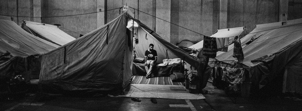 

fot. 
Angelos Tzortzinis, Grecja, z cyklu: "Trapped in Greece", częściowo finansowanego przez Fundację Magnum, nominacja w kategorii "Projekt długoterminowy" / World Press Photo 2021<br></br><br></br>

Dziesiątki tysięcy ludzi uciekających z ogarniętych wojną i biedą ojczyzn utknęło w Grecji od czasu apogeum kryzysu uchodźczego w Europie w 2016 roku. Według raportu UNHCR z marca 2016 roku, ponad milion osób, głównie uchodźców z Syrii, Iraku i Afganistanu, przekroczyło granicę Grecji od początku 2015 roku. Gdy kraje bałkańskie i europejskie na północ od Grecji zaczęły zamykać swoje granice przed napływającymi migrantami, ponad 90 000 osób pozostało uwięzionych w Grecji, w obozach lub na ulicach. Moria Reception and Identification Center na wyspie Lesbos, we wschodniej części Morza Egejskiego, był największym obozem dla uchodźców w Europie, dopóki nie spłonął w pożarze we wrześniu 2020 roku. Do lata 2020 roku około 20 000 osób mieszkało w obozie zbudowanym tak, aby pomieścić 3000 osób. Mieszkańcy skarżyli się na deszcz, zimno, choroby, brak żywności i bezpieczeństwa, niehigieniczne toalety i brak wody. Pożar, który wybuchł 9 września, prawie całkowicie zniszczył obóz. Rząd grecki powiedział, że ogień został wzniecony celowo przez migrantów protestujących przeciwko zamknięciu obozu w związku z epidemią COVID-19. Na pobliskiej wyspie Samos, pod koniec 2019 roku, prawie 8000 uchodźców mieszkało w byłej bazie wojskowej, która została zbudowana, aby pomieścić 650 osób. Mieszkańcy wyspy regularnie organizowali protesty domagając się przeniesienia obiektów na stały ląd, a mieszkańcy obozu protestowali w sprawie warunków życia. W dniu 2 listopada 2020 r. w obozie wybuchł pożar, dwa dni po tym, jak wyspę nawiedziło trzęsienie ziemi o sile 6,7 magnitudy. Od 100 do 150 osób straciło swoje domy. Fotograf od ośmiu lat zajmuje się problematyką migracji. Ten projekt - realizowany na Samos i Lesbos, a także w obozach dla uchodźców w całej Grecji - ma na celu zbadanie ludzkich i społecznych zdolności adaptacyjnych.