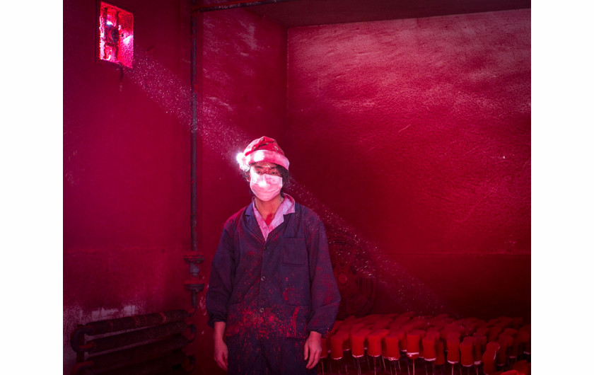 Wei, 19-letni chiński robotnik, ma na sobie maskę i świąteczną czapkę. Stoi on obok ozdób świątecznych, które są suszone na czerwony proszek stosowany do barwienia. Chiny. Fot. Ronghui Chen, Chiny, City Express