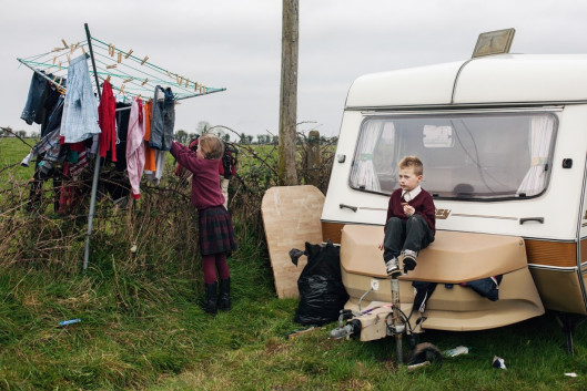 fot. Birte Kaufmann, „Travellersi”

Projekt „Travellersi” dokumentuje życie członków najliczniejszej mniejszości w Irlandii. Mowa o współczesnych nomadach wywodzących się z tradycji migracji zarobkowej. Dzisiaj cel tułaczki się zmienił, tzw. travellersi próbują na nowo odnaleźć swoją tożsamość w społeczeństwie Europy Zachodniej. Styl życia irlandzkich koczowników jest dosyć nietypowy, dlatego spotyka się z brakiem akceptacji ze strony reszty obywateli. Ci ludzie żyją jakby w równoległej rzeczywistości, która rządzi się swoimi prawami, i w której obowiązuje tradycyjny podział ról. Osoby z zewnątrz rzadko mają wstęp do tego hermetycznego świata.

Po dziś dzień niektóre rodziny rozbijają nielegalne obozowiska przy drodze. Żyją bez prądu, bieżącej wody, ani sanitariatów, choć władze zapewniają im specjalne pola kempingowe, gdzie mogą parkować swoje wozy.

Pierwszy raz do Irlandii wybrałam się VW „ogórkiem” w 2011 roku. Na zdjęciach chciałam uchwycić styl życia travellersów i wartości, którymi się kierują. Nie zamierzałam idealizować ich zwyczajów. Chciałam pokazać świat współczesnych nomadów, którzy polują na króliki, nie mogą się obejść bez koni, od dziecka zmagają się z trudami życia i walczą z nudą.

Podczas mojego pierwszego spotkania z irlandzkimi tułaczami poznałam pewną liczną rodzinę. W miarę upływu czasu zdobywałam ich zaufanie. W końcu zgodzili się, żebym z nimi zamieszkała. Ja i mój aparat staliśmy się częścią ich codziennego życia