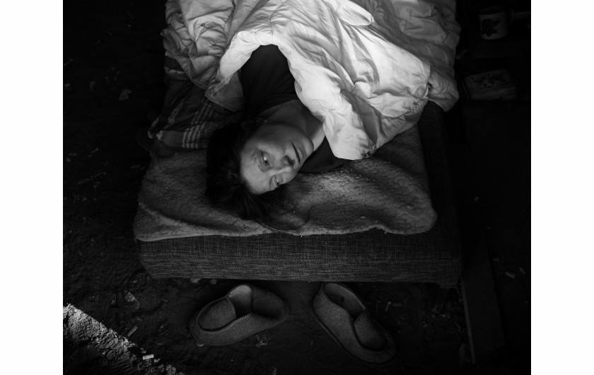 Fot. Maciej Grzybowski, 1. miejsce w kat. Documentary Project / Grand Press Photo 2024Ela, Darek i Mirek są w bezdomności od wielu lat. Mieszkają w lesie nad rzeką, na obrzeżach miasta. Opiekują się dwoma psami Florą i Jogim. Ela przez kilkanaście lat pracowała w zakładach farmaceutycznych. Jest wdową, jej syn mieszka za granicą. Obecnie bezrobotna. Darek, partner Eli, podejmuje się prac dorywczych na budowach i w firmach sprzątających miasto. Sam zbudował wszystkie domki. Mirek pochodzi z Pomorza, jest wolnym duchem. Często wychodzi w nocy zbierać złom, który potem sprzedaje.
W Polsce około 30 tysięcy osób znajduje się w kryzysie bezdomności, z czego ponad 80 proc. stanowią mężczyźni.

