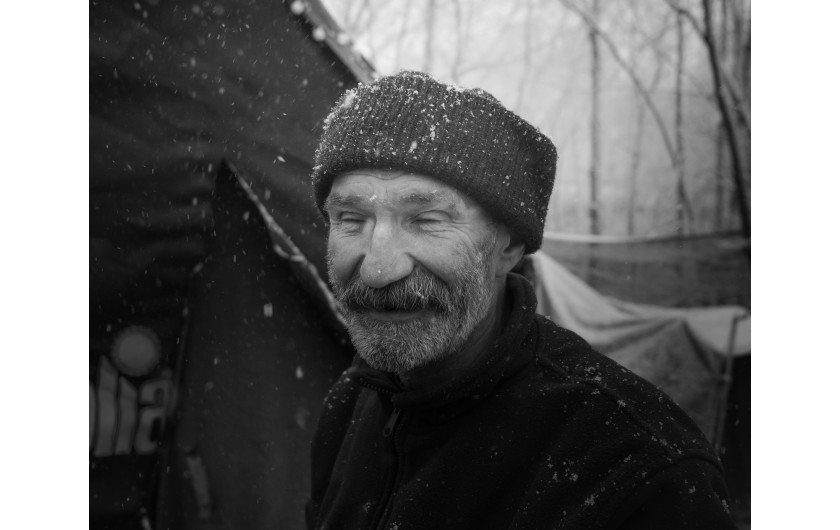 Fot. Maciej Grzybowski, 1. miejsce w kat. Documentary Project / Grand Press Photo 2024Ela, Darek i Mirek są w bezdomności od wielu lat. Mieszkają w lesie nad rzeką, na obrzeżach miasta. Opiekują się dwoma psami Florą i Jogim. Ela przez kilkanaście lat pracowała w zakładach farmaceutycznych. Jest wdową, jej syn mieszka za granicą. Obecnie bezrobotna. Darek, partner Eli, podejmuje się prac dorywczych na budowach i w firmach sprzątających miasto. Sam zbudował wszystkie domki. Mirek pochodzi z Pomorza, jest wolnym duchem. Często wychodzi w nocy zbierać złom, który potem sprzedaje.
W Polsce około 30 tysięcy osób znajduje się w kryzysie bezdomności, z czego ponad 80 proc. stanowią mężczyźni.
