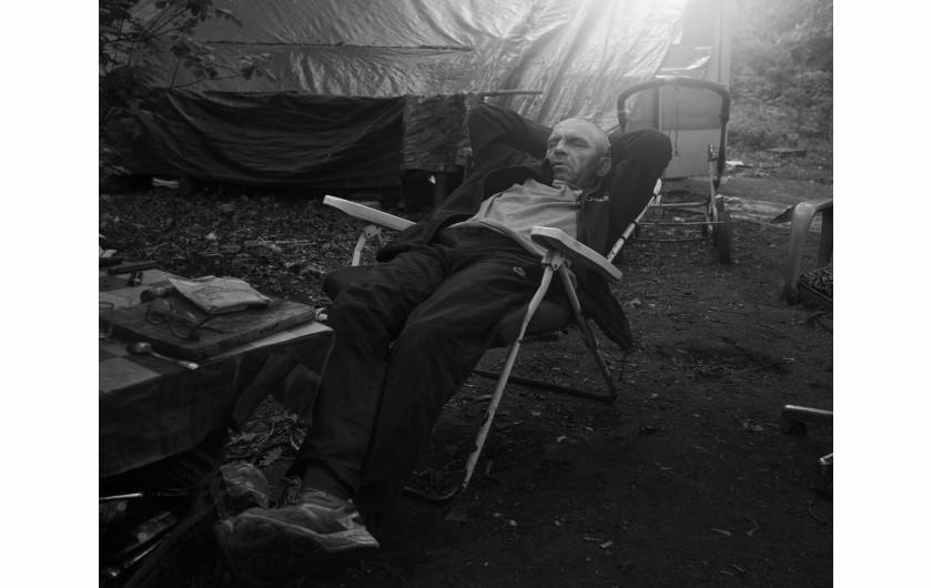 Fot. Maciej Grzybowski, 1. miejsce w kat. Documentary Project / Grand Press Photo 2024Ela, Darek i Mirek są w bezdomności od wielu lat. Mieszkają w lesie nad rzeką, na obrzeżach miasta. Opiekują się dwoma psami Florą i Jogim. Ela przez kilkanaście lat pracowała w zakładach farmaceutycznych. Jest wdową, jej syn mieszka za granicą. Obecnie bezrobotna. Darek, partner Eli, podejmuje się prac dorywczych na budowach i w firmach sprzątających miasto. Sam zbudował wszystkie domki. Mirek pochodzi z Pomorza, jest wolnym duchem. Często wychodzi w nocy zbierać złom, który potem sprzedaje.
W Polsce około 30 tysięcy osób znajduje się w kryzysie bezdomności, z czego ponad 80 proc. stanowią mężczyźni.
