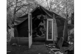 Fot. Maciej Grzybowski, 1. miejsce w kat. Documentary Project / Grand Press Photo 2024<br></br><br></br>Ela, Darek i Mirek są w bezdomności od wielu lat. Mieszkają w lesie nad rzeką, na obrzeżach miasta. Opiekują się dwoma psami Florą i Jogim. Ela przez kilkanaście lat pracowała w zakładach farmaceutycznych. Jest wdową, jej syn mieszka za granicą. Obecnie bezrobotna. Darek, partner Eli, podejmuje się prac dorywczych na budowach i w firmach sprzątających miasto. Sam zbudował wszystkie domki. Mirek pochodzi z Pomorza, jest wolnym duchem. Często wychodzi w nocy zbierać złom, który potem sprzedaje.
W Polsce około 30 tysięcy osób znajduje się w kryzysie bezdomności, z czego ponad 80 proc. stanowią mężczyźni.
