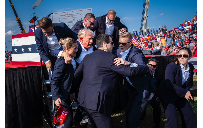 Fot. Jabin Botsford, The Washington Post, Attempted Assassination of Donald Trump, nagroda w kat. regionalnej North & Central America / World Press Photo 2025Agenci Secret Service pomagają republikańskiemu kandydatowi na prezydenta Donaldowi Trumpowi zejść ze sceny chwilę po tym, jak kula zamachowca trafiła go w ucho podczas wiecu wyborczego. Butler, Pensylwania, Stany Zjednoczone, 13 lipca 2024 r.
Uważa się, że próba zamachu na Donalda Trumpa i związane z nią doniesienia medialne stanowiły punkt zwrotny w kampanii prezydenckiej, który ukształtował nie tylko nadchodzące wybory, ale także polityczną przyszłość USA. Tuż po strzelaninie republikański kandydat na prezydenta w 2024 roku wyzywająco krzyczał: „Walczcie, walczcie, walczcie!”. Warto zauważyć, że ten obraz, uchwycony kilka sekund później, przedstawia rzadki i szczery moment kruchości w kampanii, która koncentrowała się na witalności i sile.