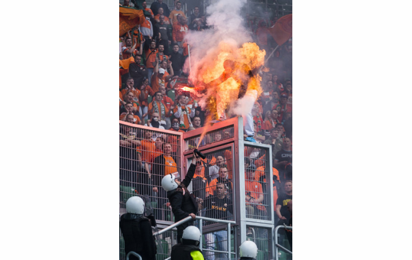 II miejsce w kat. WYDARZENIA, fot. Sebastian Borowski, „Fakt” Wrocław. Podczas derbów Śląsk Wrocław – KGHM Zagłębie Lubin na stadionie miejskim kibice odpalali race. Jeden z kibiców Lubina szczególnie się wyróżniał: wchodził na ogrodzenie, machał zapaloną racą w kierunku stewardów. Był zamaskowany. Gdy obok trybun pojawił się szpaler ochroniarzy, jeden miał w ręce coś na kształt gaśnicy, lecz jak się okazało, był to gaz pieprzowy. Gdy go użył, w zetknięciu z racą niespodziewanie powstał pożar i kibic na moment zapłonął jak pochodnia. Nie doznał obrażeń; przed poparzeniem twarzy uchroniła go kominiarka. 26 kwietnia 2014 