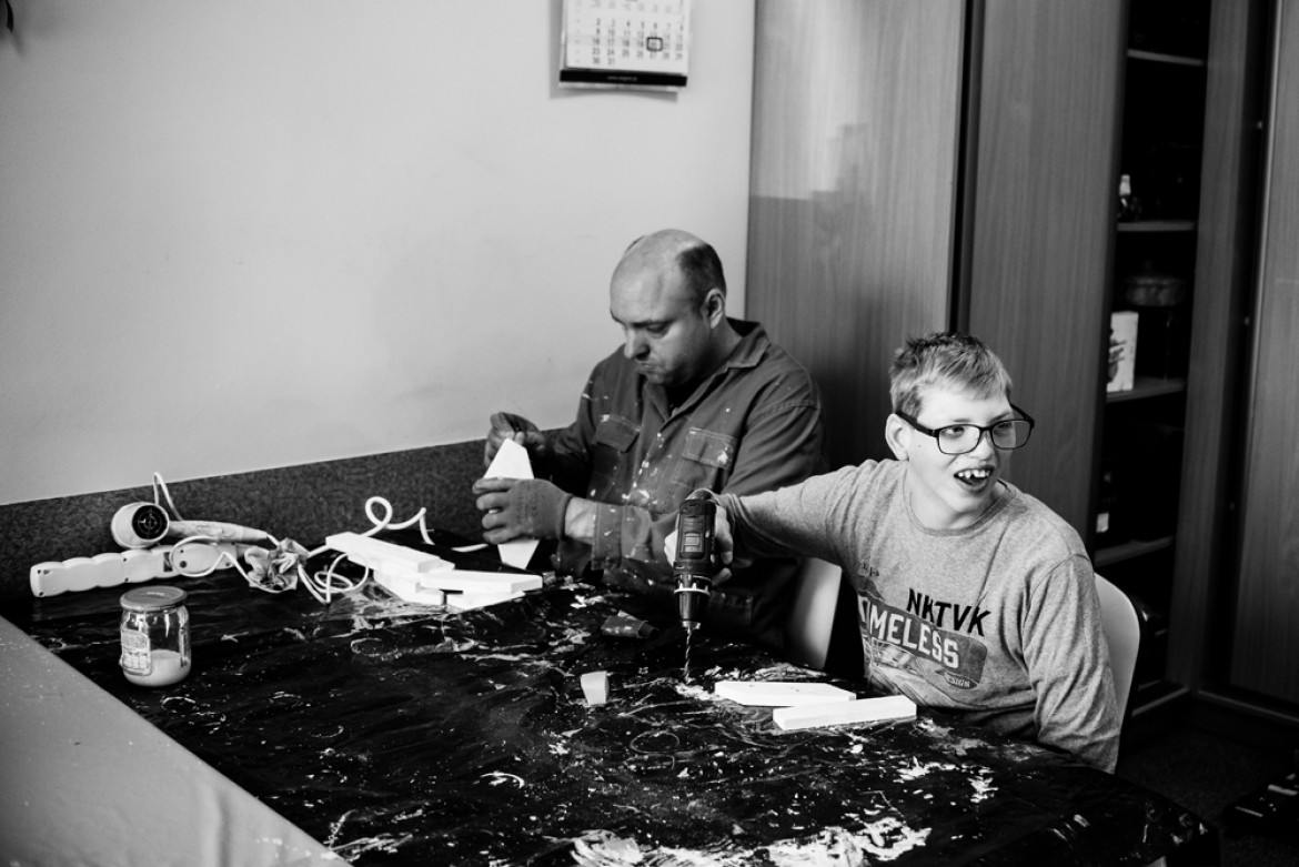 fot. Dawid Stube, I miejsce w kategorii Projekt Dokumentalny
Gniezno, Jarosławiec. Igor ma 19 lat. Chłopcy w tym wieku zaczynają czerpać garściami z życia: dojrzewają, przeżywają pierwsze bunty, pierwsze miłości, odkrywają świat. Igor nie ma tego. Cierpi na rzadką chorobę genetyczną: zespół kociego krzyku. Codziennie wraz z matką walczą o to, by odkrywany przez niego świat choć trochę przypominał ten normalny. Na początku właśnie pokazanie takiego świata było dla mnie celem projektu. Jednak im dłużej fotografowałem, tym bardziej wyłaniał mi się obraz dwojga ludzi, którzy mimo olbrzymich problemów w codziennej walce zbudowali ze sobą potężną więź: między matką a synem. Filarem tej więzi jest miłość. Ta głęboka relacja daje im siłę.
Z projektu, który był budowany przez cztery lata, wyłania się przede wszystkim obraz niezwykłej pielęgnacji miłości. Ale także obraz chłopca samotnego, zagubionego. W tle jednak zawsze jest czuwająca nad nim matka. Ona jest dla niego filarem, na którym może się oprzeć w trudnej codzienności – a on dla niej.