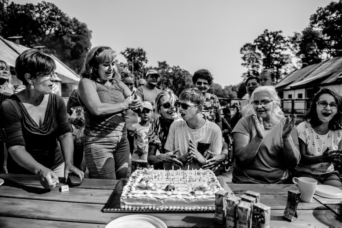 fot. Dawid Stube, I miejsce w kategorii Projekt Dokumentalny
Gniezno, Jarosławiec. Igor ma 19 lat. Chłopcy w tym wieku zaczynają czerpać garściami z życia: dojrzewają, przeżywają pierwsze bunty, pierwsze miłości, odkrywają świat. Igor nie ma tego. Cierpi na rzadką chorobę genetyczną: zespół kociego krzyku. Codziennie wraz z matką walczą o to, by odkrywany przez niego świat choć trochę przypominał ten normalny. Na początku właśnie pokazanie takiego świata było dla mnie celem projektu. Jednak im dłużej fotografowałem, tym bardziej wyłaniał mi się obraz dwojga ludzi, którzy mimo olbrzymich problemów w codziennej walce zbudowali ze sobą potężną więź: między matką a synem. Filarem tej więzi jest miłość. Ta głęboka relacja daje im siłę.
Z projektu, który był budowany przez cztery lata, wyłania się przede wszystkim obraz niezwykłej pielęgnacji miłości. Ale także obraz chłopca samotnego, zagubionego. W tle jednak zawsze jest czuwająca nad nim matka. Ona jest dla niego filarem, na którym może się oprzeć w trudnej codzienności – a on dla niej.