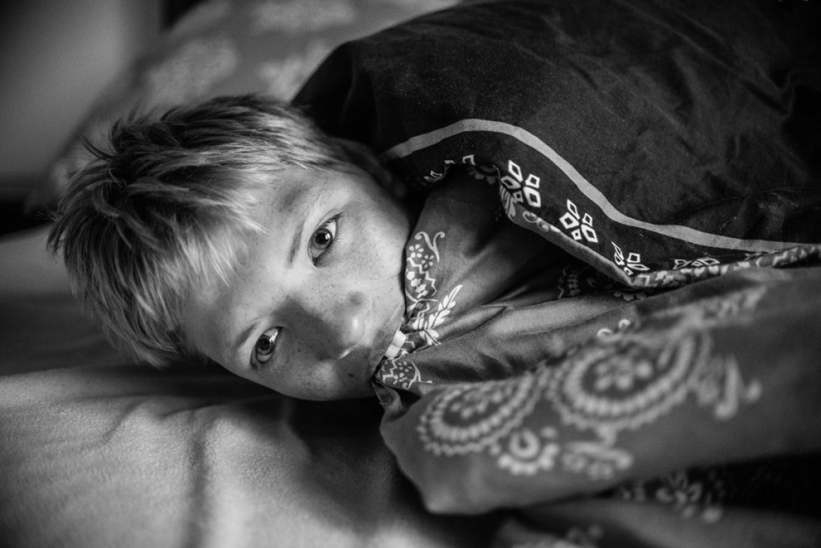 fot. Dawid Stube, I miejsce w kategorii Projekt Dokumentalny
Gniezno, Jarosławiec. Igor ma 19 lat. Chłopcy w tym wieku zaczynają czerpać garściami z życia: dojrzewają, przeżywają pierwsze bunty, pierwsze miłości, odkrywają świat. Igor nie ma tego. Cierpi na rzadką chorobę genetyczną: zespół kociego krzyku. Codziennie wraz z matką walczą o to, by odkrywany przez niego świat choć trochę przypominał ten normalny. Na początku właśnie pokazanie takiego świata było dla mnie celem projektu. Jednak im dłużej fotografowałem, tym bardziej wyłaniał mi się obraz dwojga ludzi, którzy mimo olbrzymich problemów w codziennej walce zbudowali ze sobą potężną więź: między matką a synem. Filarem tej więzi jest miłość. Ta głęboka relacja daje im siłę.
Z projektu, który był budowany przez cztery lata, wyłania się przede wszystkim obraz niezwykłej pielęgnacji miłości. Ale także obraz chłopca samotnego, zagubionego. W tle jednak zawsze jest czuwająca nad nim matka. Ona jest dla niego filarem, na którym może się oprzeć w trudnej codzienności – a on dla niej.