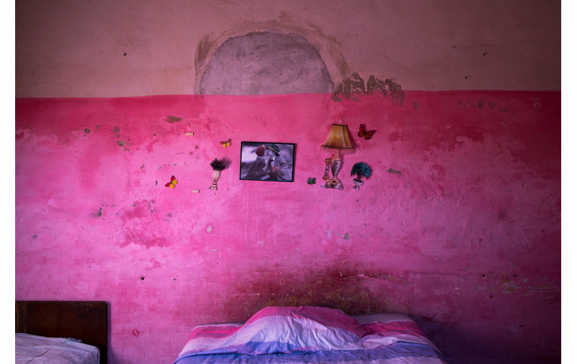 fot. Oded Wagenstein, Kolorowe przedmioty przyklejone na ścianie w jednopokojowych mieszkaniu starzejącej się społeczności, Cienfuegos, Kuba, Grudzień 2016. Kiedy umiera najemca, samorząd lokuje w mieszkaniu innego dzierżawcę i maluje ściany na nowo.