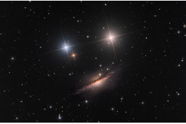 fot. Nicolas Rolland, Martin Pugh, "A Smiley in Space", 3. miejsce w kat. Galaxies<br></br><br></br>- NGC 1055 to galaktyka spiralna z wyraźnym zgrubieniem jądrowym, przecinanym przez ciemne pasmo gazu i pyłu – mówią zwycięzcy. - Kolorowe gwiazdy wokół NGC 1055 są na pierwszym planie, wewnątrz Drogi Mlecznej. Wyglądają jak oczy kosmicznej buźki.